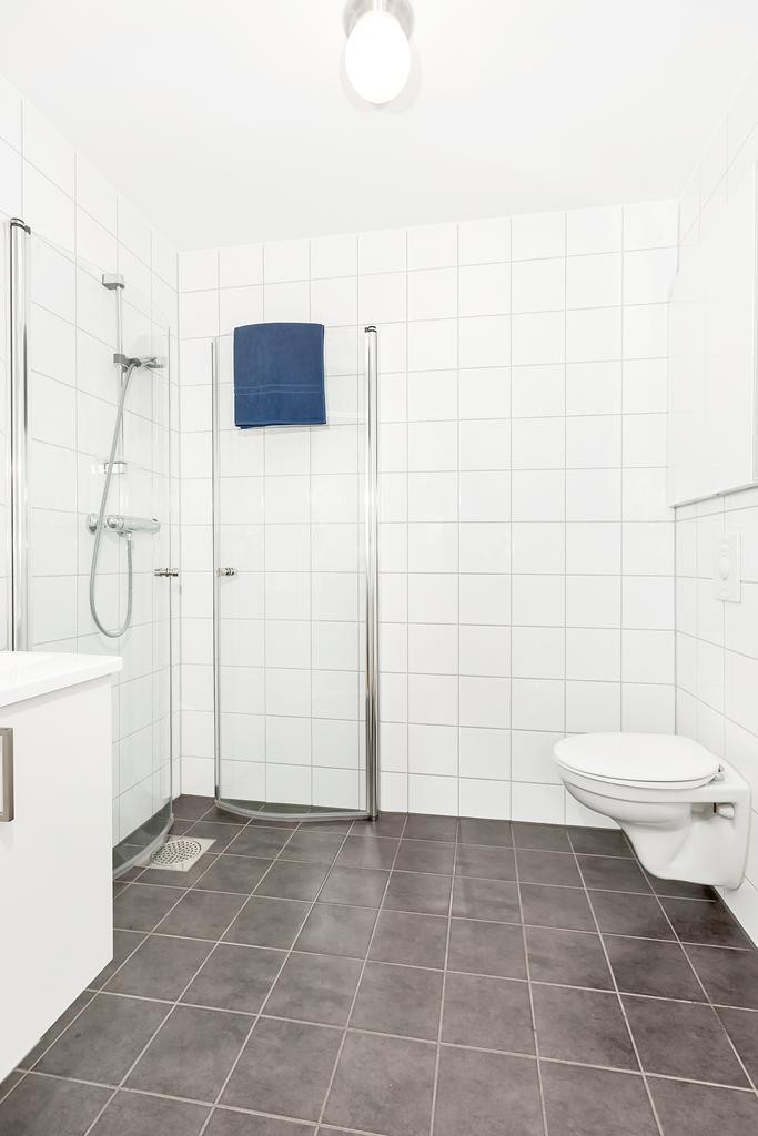 Badene har pen innredning med hvite baderomsseksjoner, dusjhjørner i glass og vegghengt toalett Galleribilde