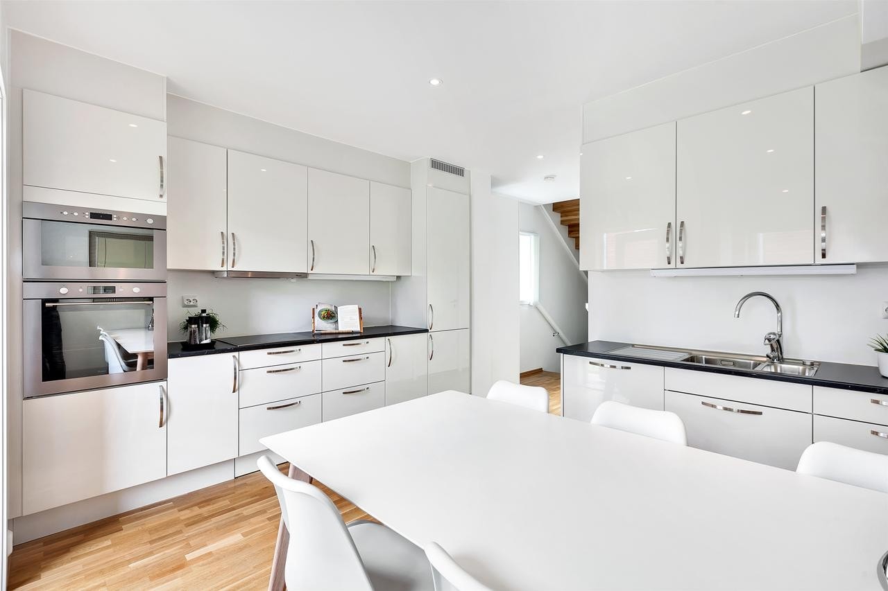 Kjøkkenet har stilrene fronter i hvit høyglans og mørk laminert benkeplate Galleribilde