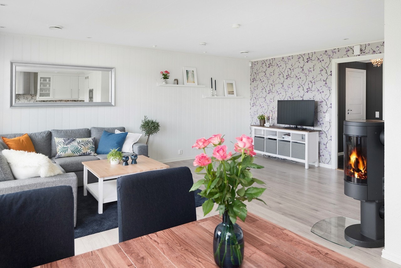 Stuen har lysmalte veggflater pent oppbrudd av en fondvegg med mønstret tapet. Galleribilde