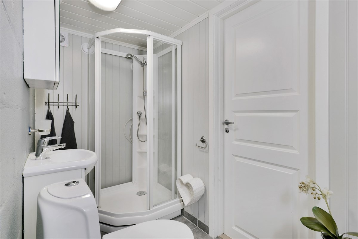 Badet i kjelleretasjen er lyst og trivelig med grå gulvfliser og grå vegger i en kombinasjon av mur og panel. Innredningen består av heldekkende servant på underskap med hvite fronter, speilskap og belysning. Galleribilde