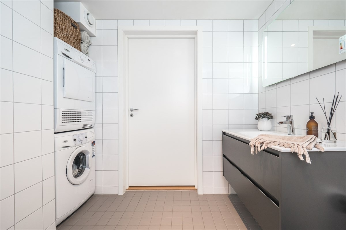 Badet inneholder dusjhjørne med dusj på vegg, vegghengt toalett, servant i møbel og nisje til vaskesøyle Galleribilde