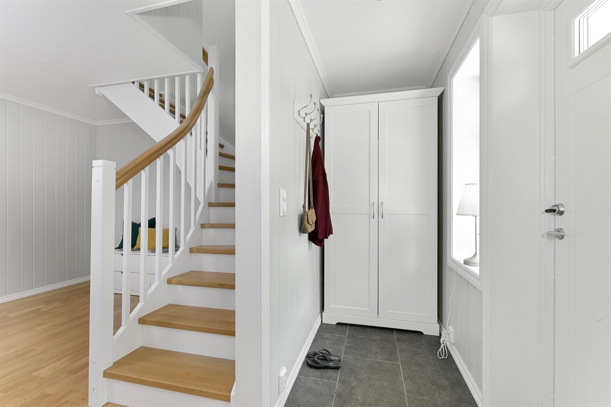 Fra entreen kommer du videre inn i en romslig trappehall med parkettgulv, holdt i samme stil som entreen med malt veggpanel, gulvvarme og downlights. Galleribilde