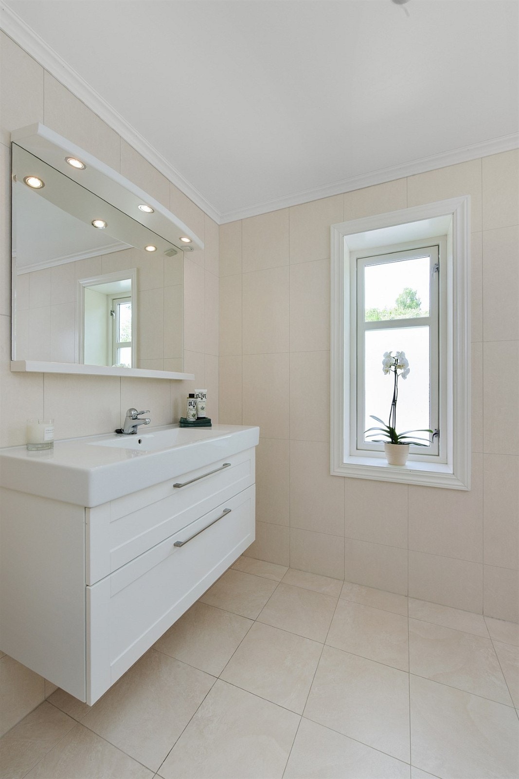 Innredningen har hvite, profilerte skuffefronter, heldekkende servant og speil med belysning i overkant. Badet har ellers veggmontert toalett og dusjhjørne med skyvedører. Galleribilde