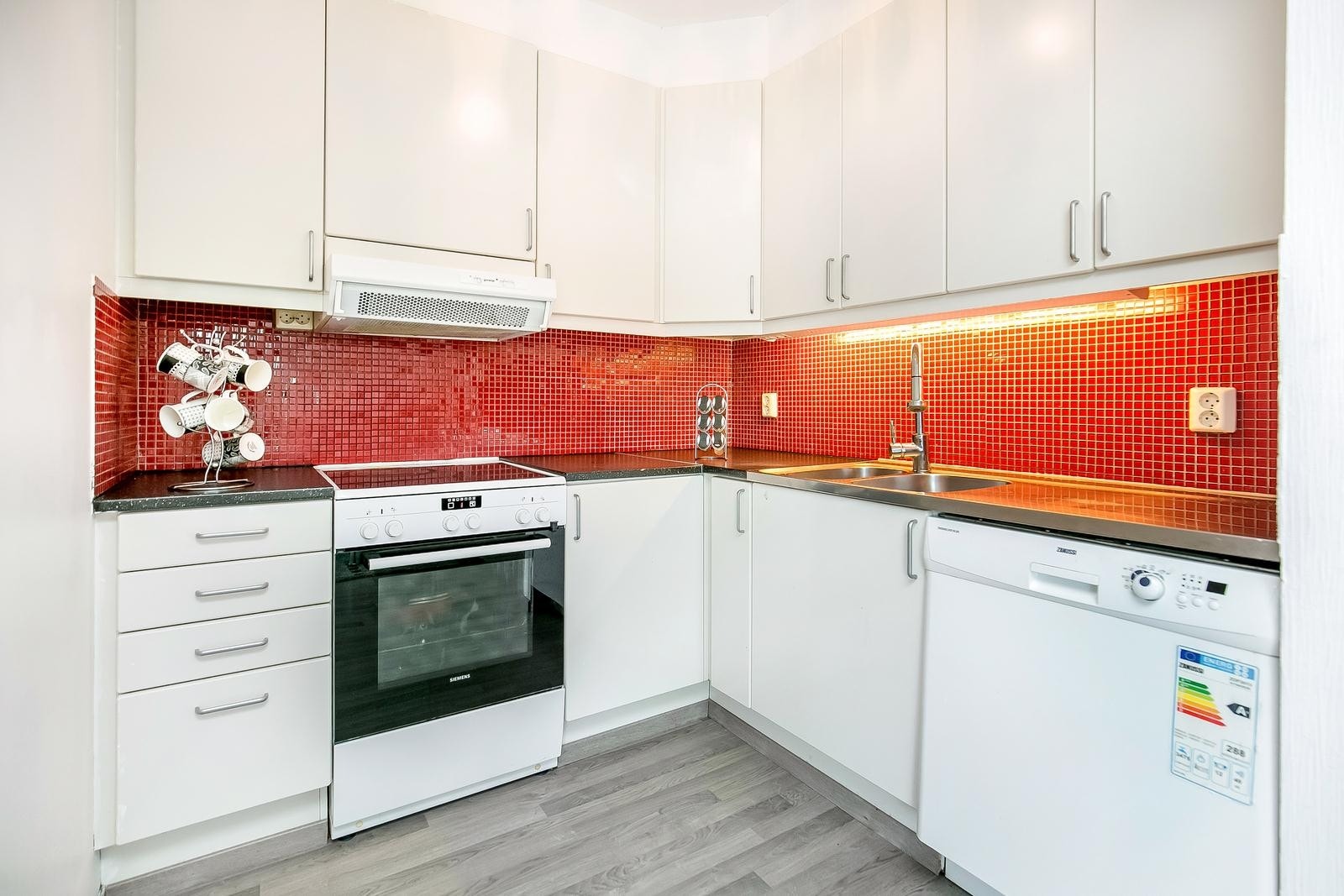 Praktisk kjøkken med slette lakkerte skapfronter i mosaikksfliser på bakvegg Galleribilde