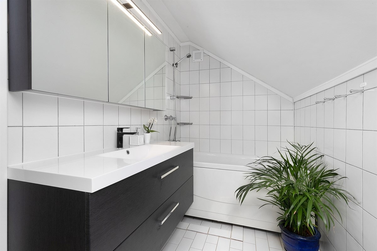 Badet i andre etasje har lyse fliser, gulvvarme og takvindu. Innredningen består av en nyere seksjon med skuffer og heldekkende servant, speilskap med lys, og veggmonterte skap. Galleribilde