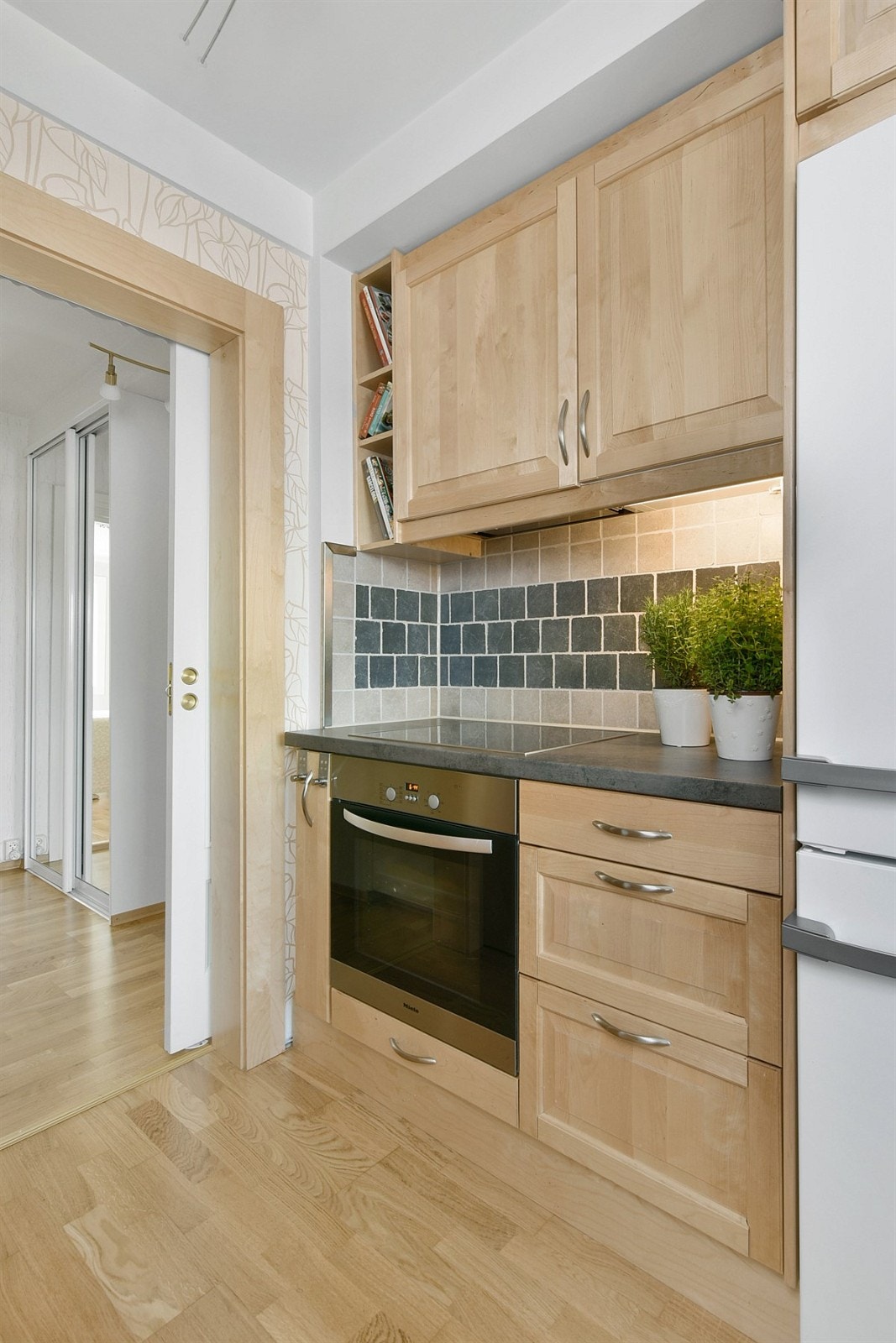 Over benken er veggen flissatt. Av hvitevarer medfølger stekeovn, induksjonstopp, oppvaskmaskin, ventilator og nisje med kombinert kjøl/frys. I tillegg er det opplegg for vaskemaskin. Galleribilde