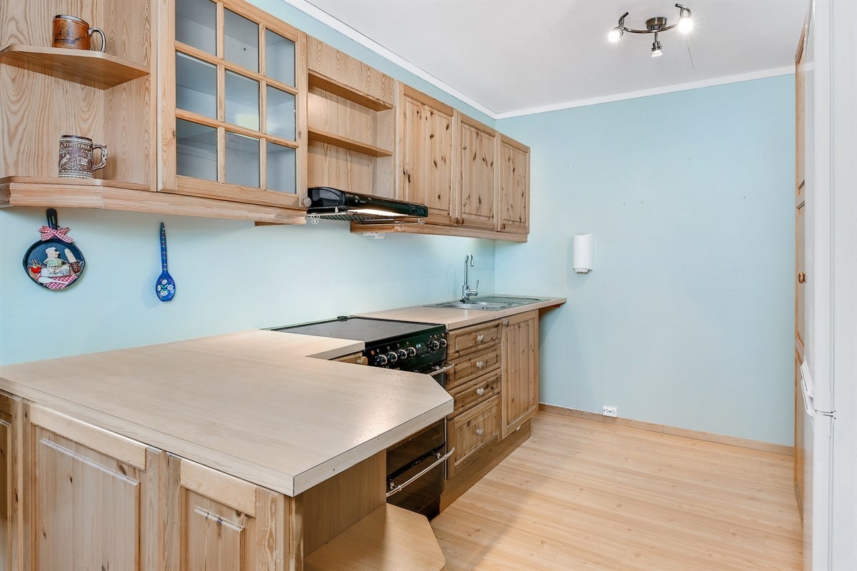 Kjøkkenet har en innredning med profilerte furufronter, vitrineskap og laminatbenkeplate med dobbel vaskekum Galleribilde