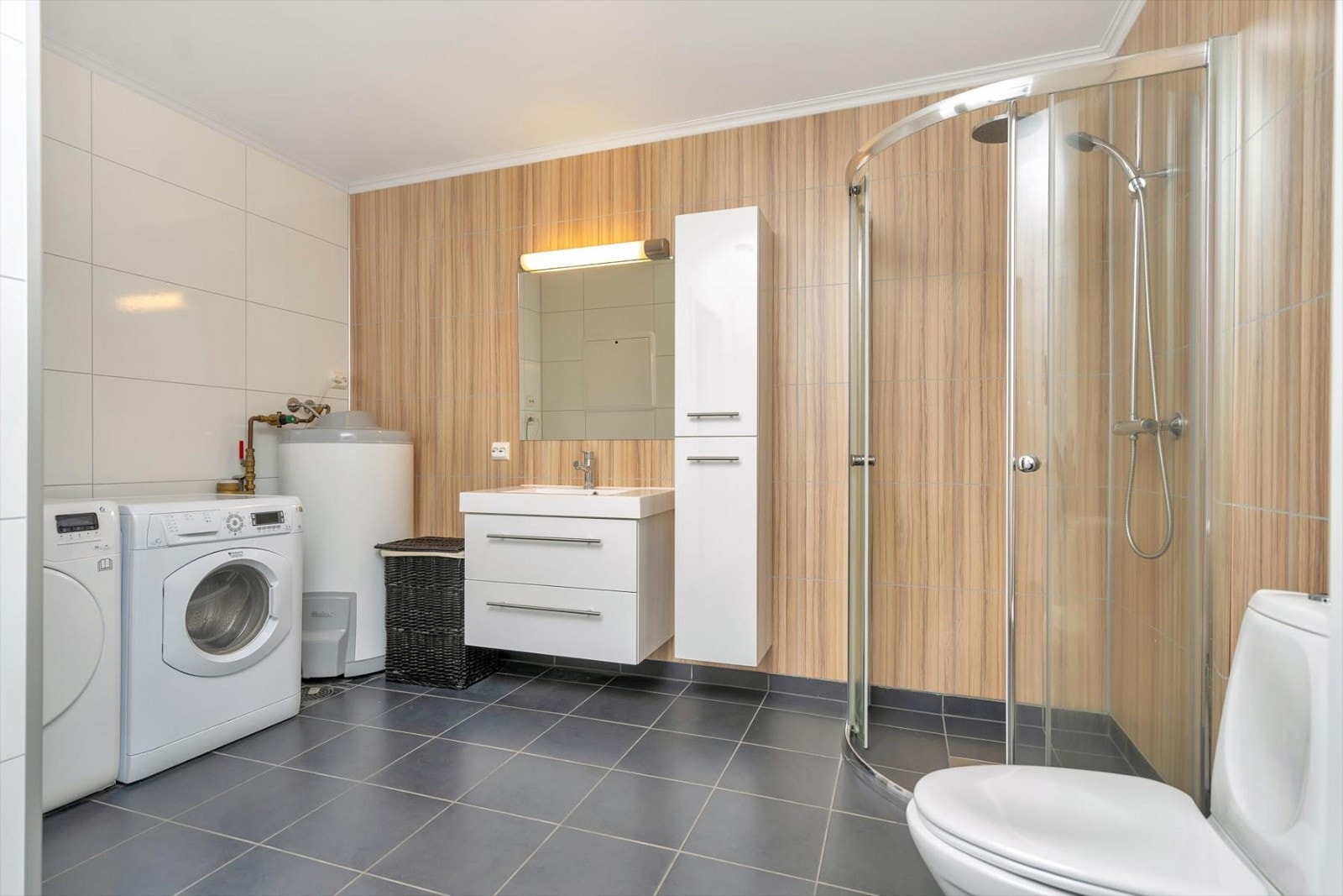 Lekkert bad med flis på gulv og våtromsplater på vegg. Dusjnisje, servant med underskuffer og sideskap, wc, mekanisk avtrekk og varmekabler i gulv. Opplegg for vaskemaskin og tørketrommel. Galleribilde