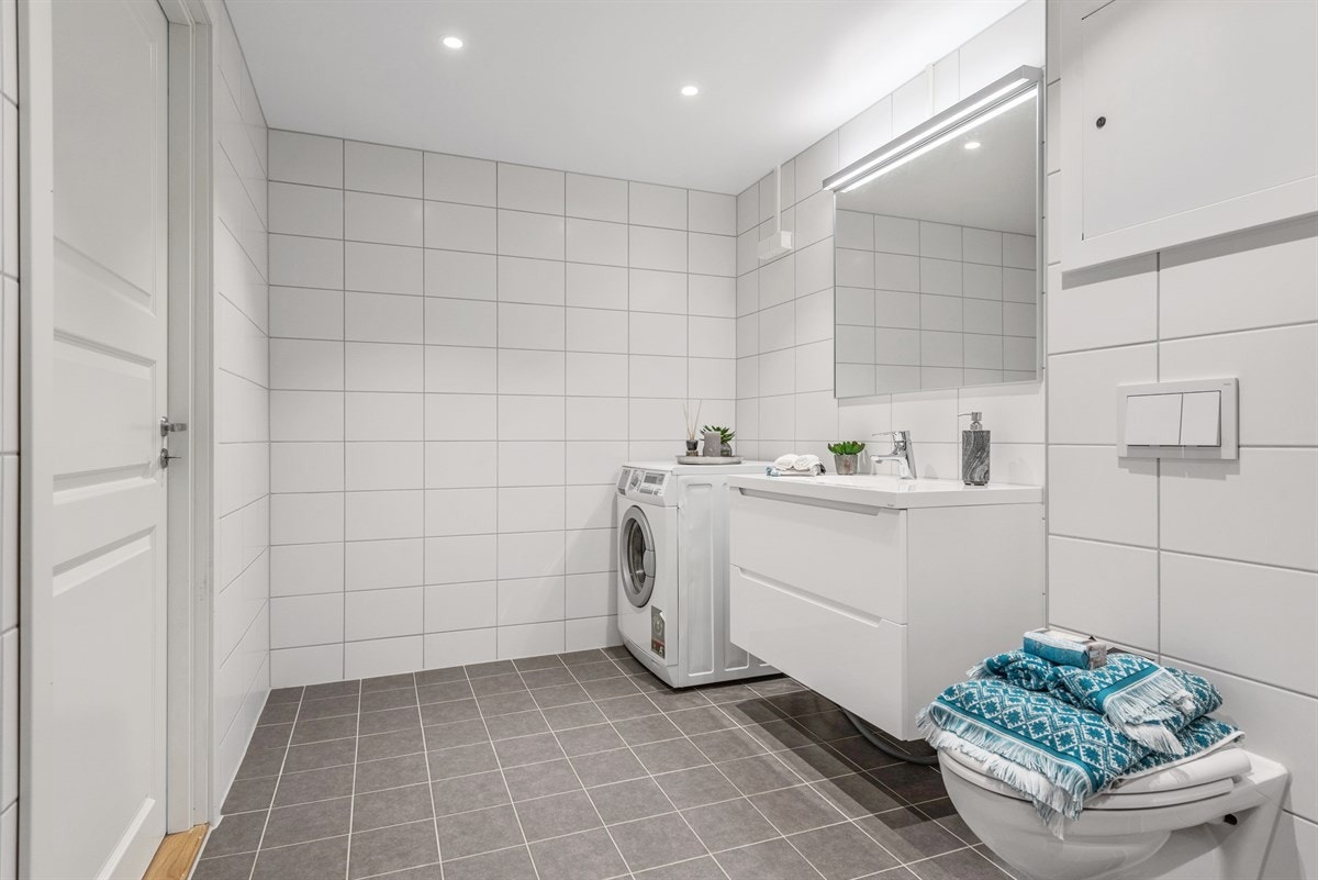 Badet er av god størrelse, oppleves romslig og inneholder dusj, vegghengt toalett, servant i skap, speil og opplegg for vaskemaskin. Galleribilde