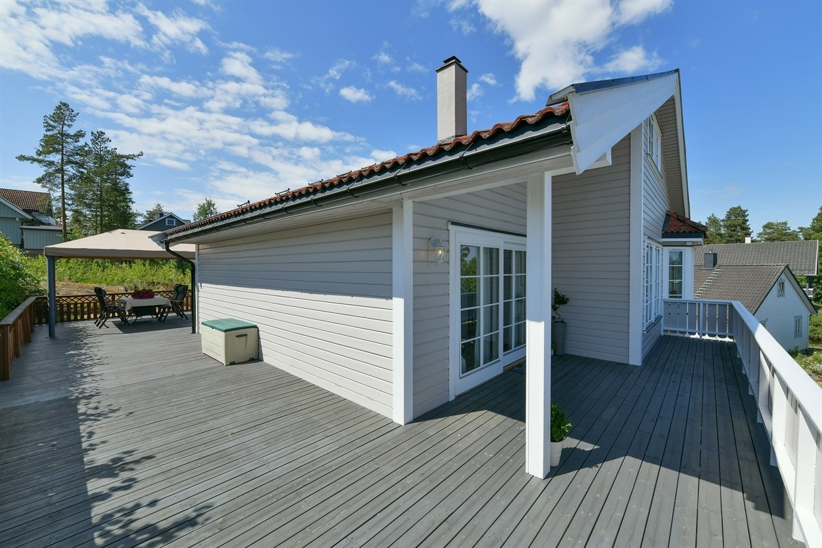 Langs tre sider av boligen ligger er herlig terrasse på hele 103 kvm med mørkbeiset trebord, lysmalt rekkverk og trapp ned til hagen. Galleribilde