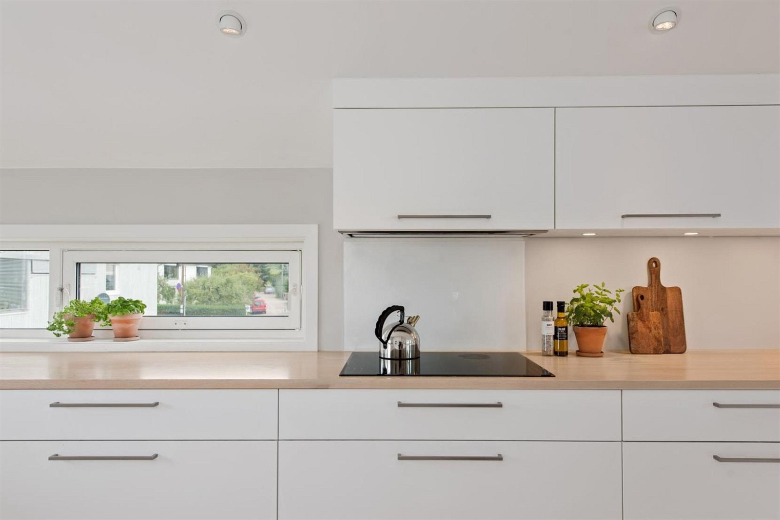 Hvit, mattlakket kjøkkeninnredningen med glatte skapdører og skuffefronter. Takhøye overskap med god belysning under skapene. Galleribilde