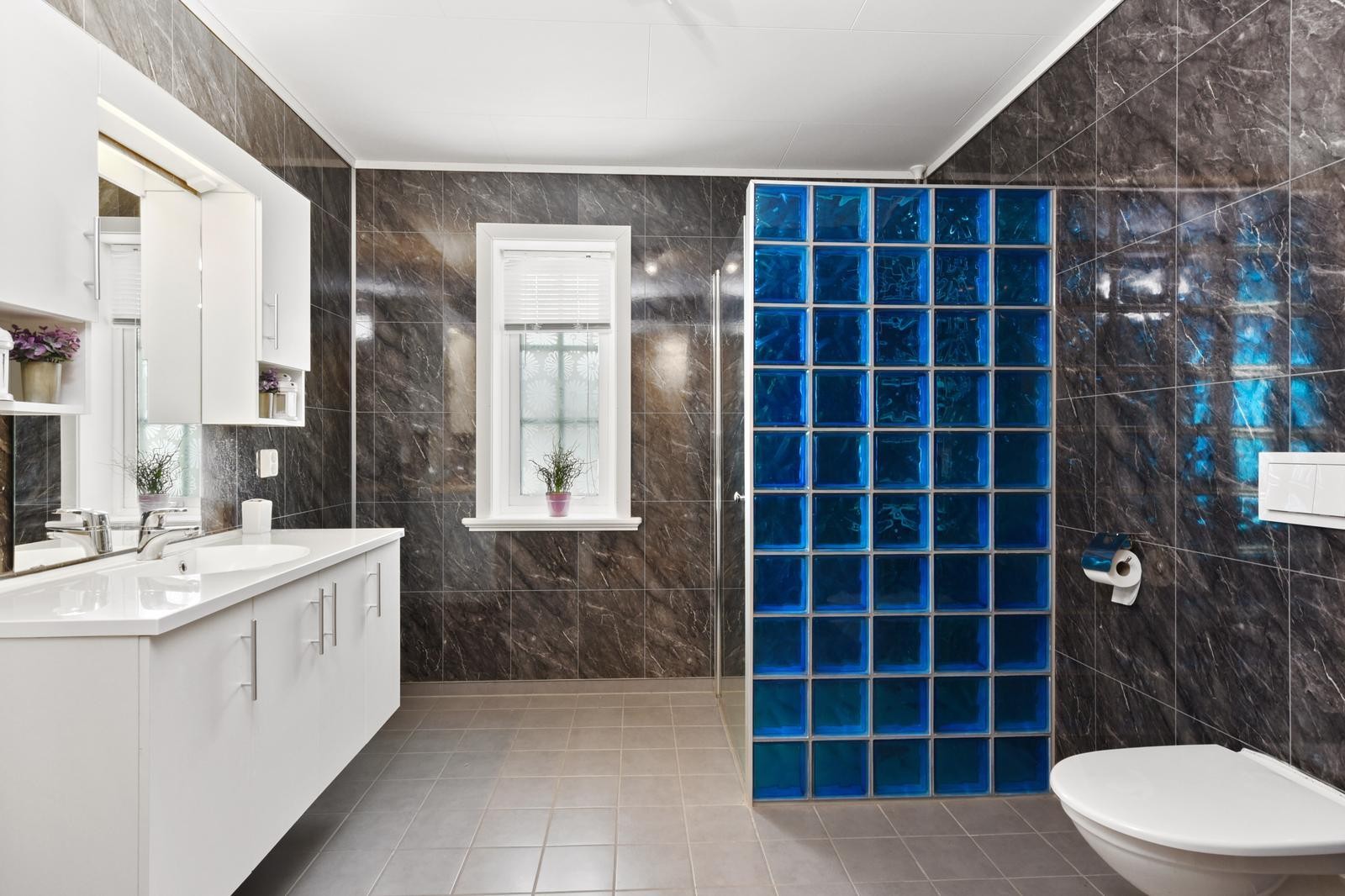 Badet har flis på gulv og våtromsplater på vegger. Det er montert innebygd toalett og dusjhjørne. Galleribilde