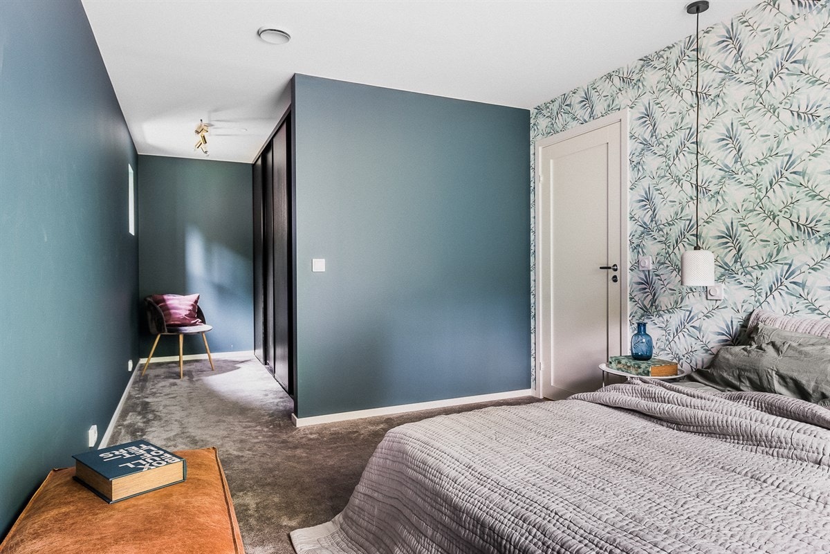 Et elegant soverom som er tapetsert med en pen kontrastvegg og ellers malt i en mørk blå farge. Galleribilde