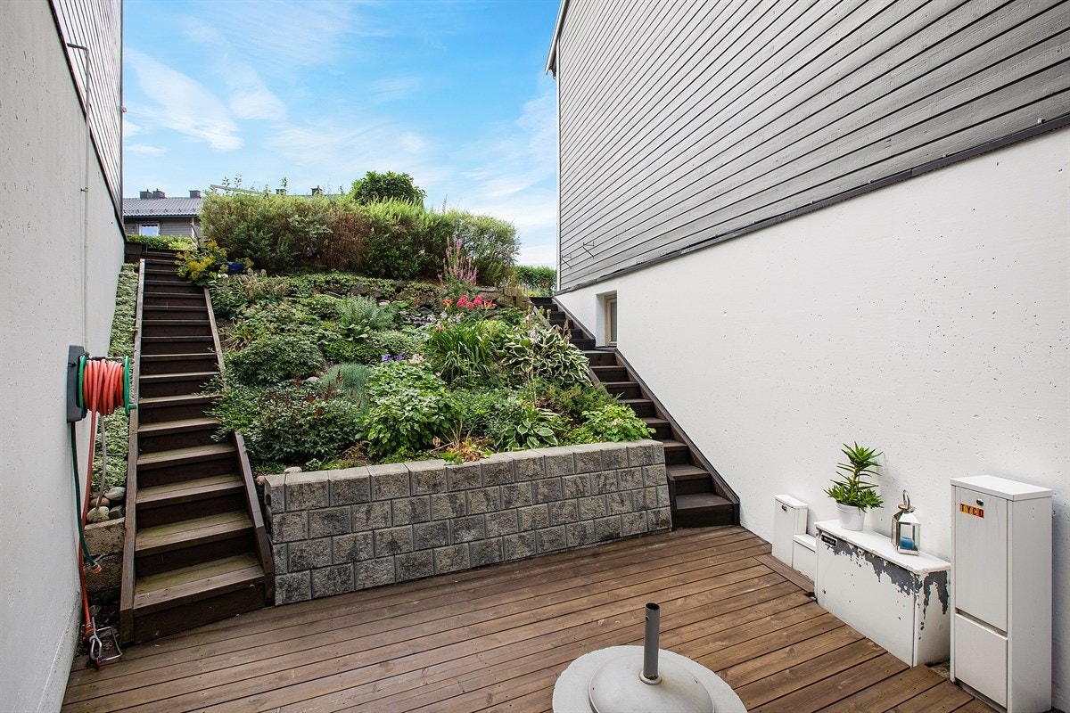 Endebeliggenheten gir mye godt areal også på gavelside. Her finnes et praktisk faststøpt tørkestativ som deles med naboen. Trappeløpet tar deg opp til hagen og terrasseplattingen. Galleribilde