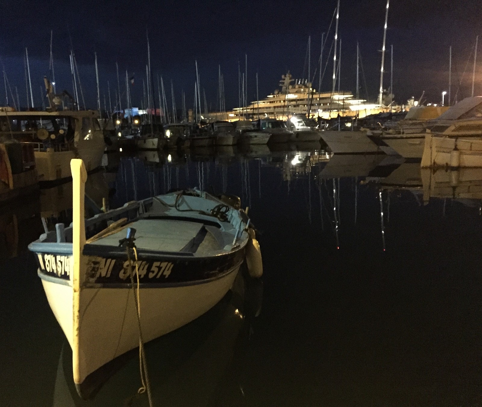 Bitteliten fiskebåt i forgrunnen, mens verdens største yacht skimtes lenger bak i havnen i Antibes Galleribilde