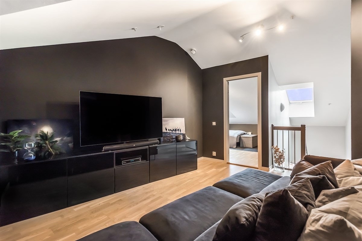 Rommet er innredet i delikate mørke overflater som gir et særpreg. Her er det plass til stor sofa, sofabord og medievegg. Galleribilde