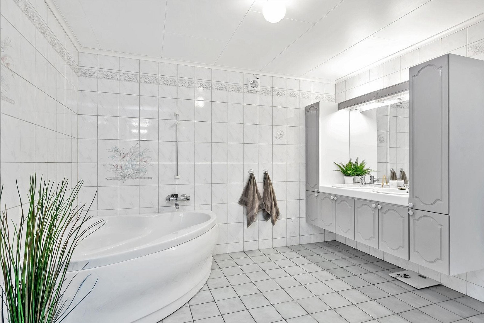 Badet har praktisk dusjhjørne, hjørnekar, toalett og lys innredning med 2 vasker. Galleribilde