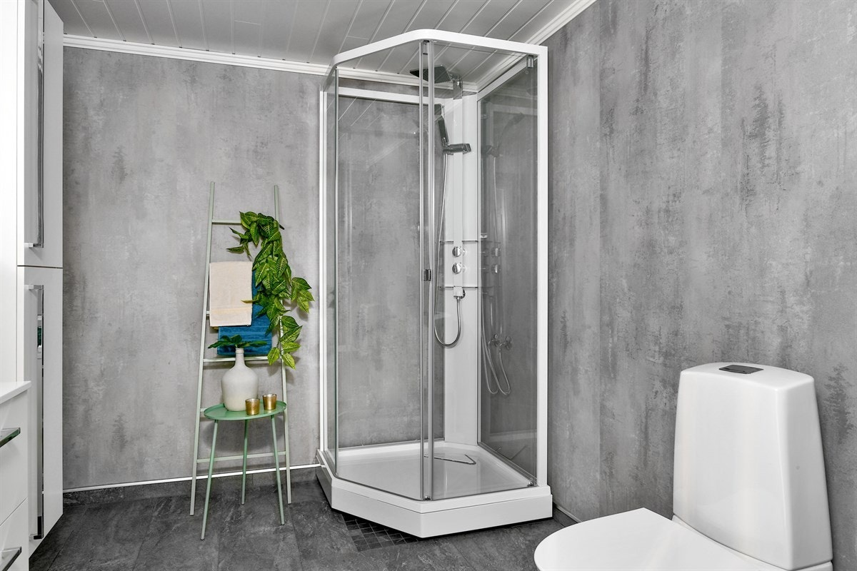 Badet har mørkegrå gulvfliser som harmonerer utmerket mot våtromsplater i moderne betongimitasjon. Galleribilde