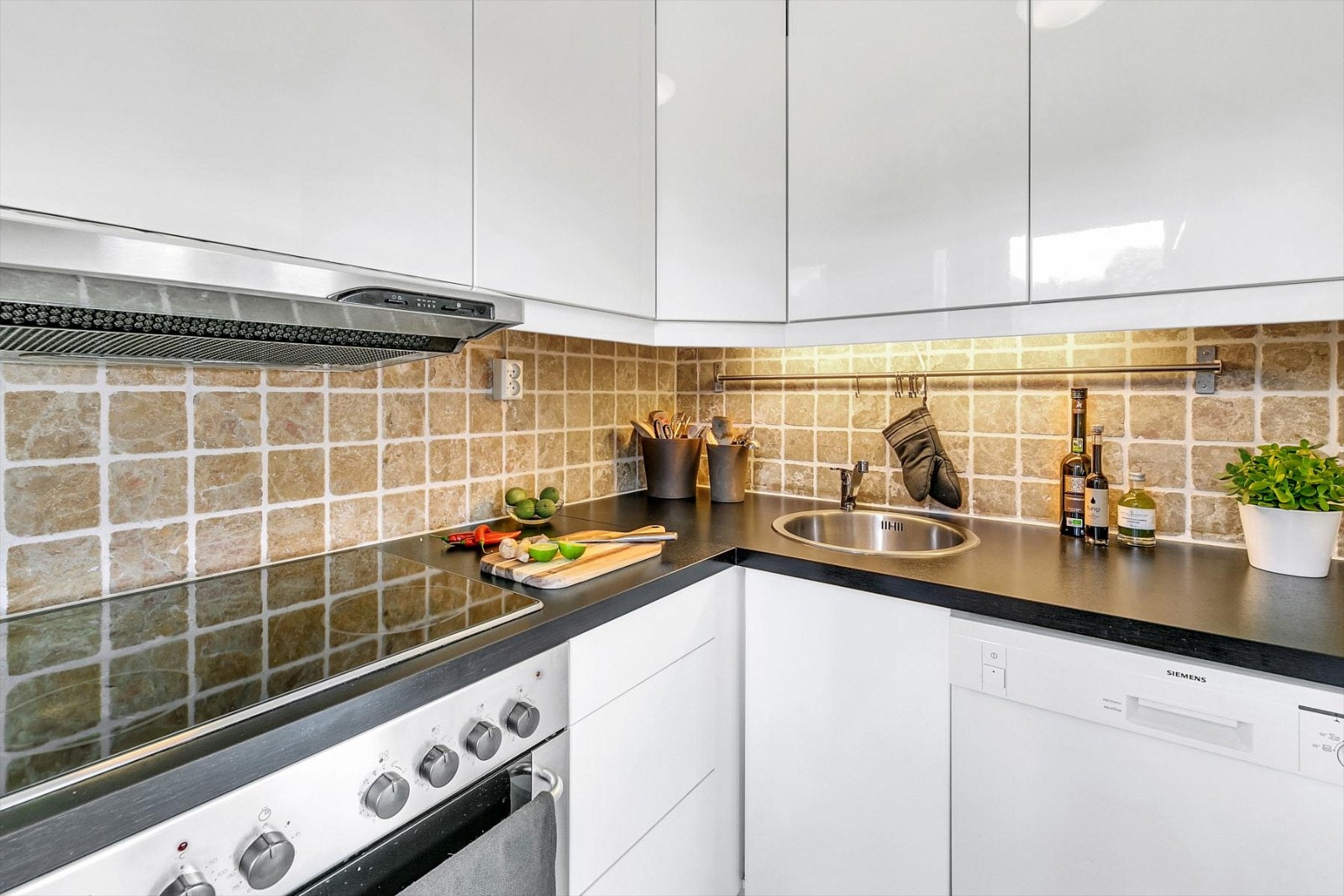 Fliser over kjøkkenbenk gjør det enkelt å holde overflaten ren. Alle hvitevarene, bortsett fra kjøl/fryseskap, er integrert for et helheltlig og moderne uttrykk (koketopp, komfyr, oppvaskmaskin). Galleribilde