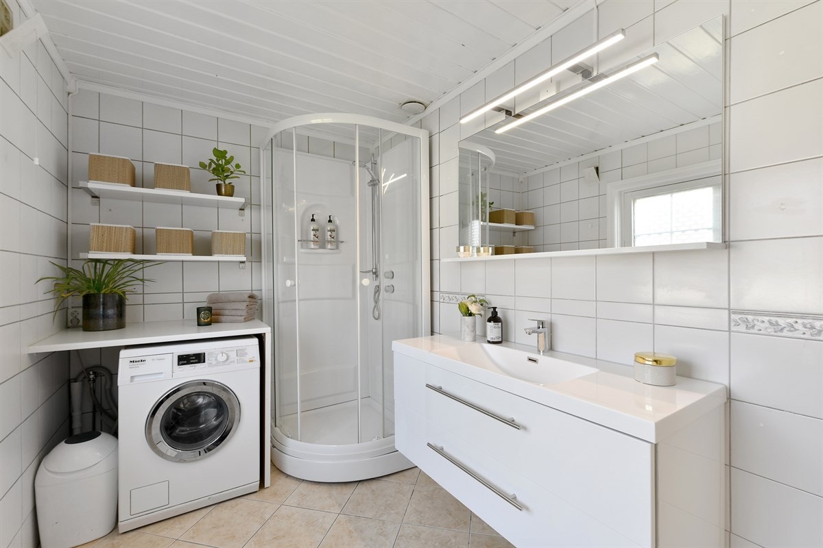 Badet ligger i første etasje og har hvite fliser på vegger og sandfargede fliser på gulv. Galleribilde