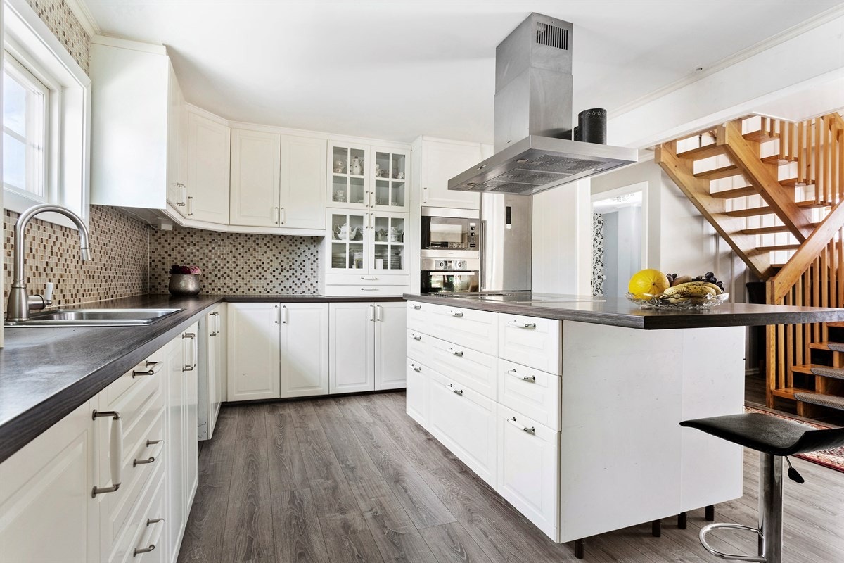 Lekkert hjørnekjøkken med folierte fronter, laminat benkeplate, mosaikkfliser over kjøkkenbenk og integrert dobbel oppvaskkum med ettgreps blandebatteri Galleribilde