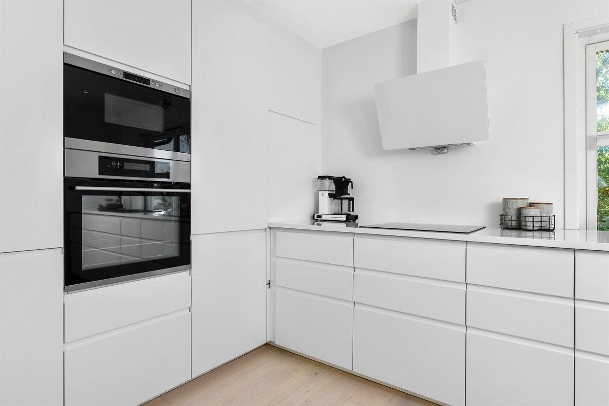 Innredningen har hvite, glatte fronter med integrerte håndtak, og hvit laminatbenkeplate med nedfelt oppvaskkum. Galleribilde