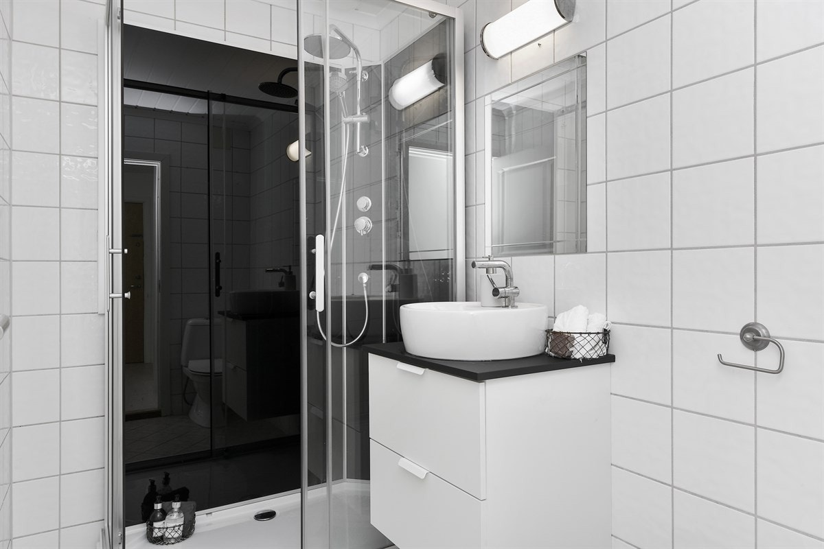 Badet er smakfullt innredet med sandfargede gulvfliser og hvite veggfliser, pent alternert med sorte veggfliser i dusjsone. Galleribilde