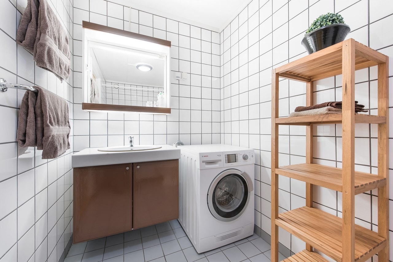 Flislagt bad med innredning og overspeil med belysning, samt opplegg for vaskemaskin Galleribilde