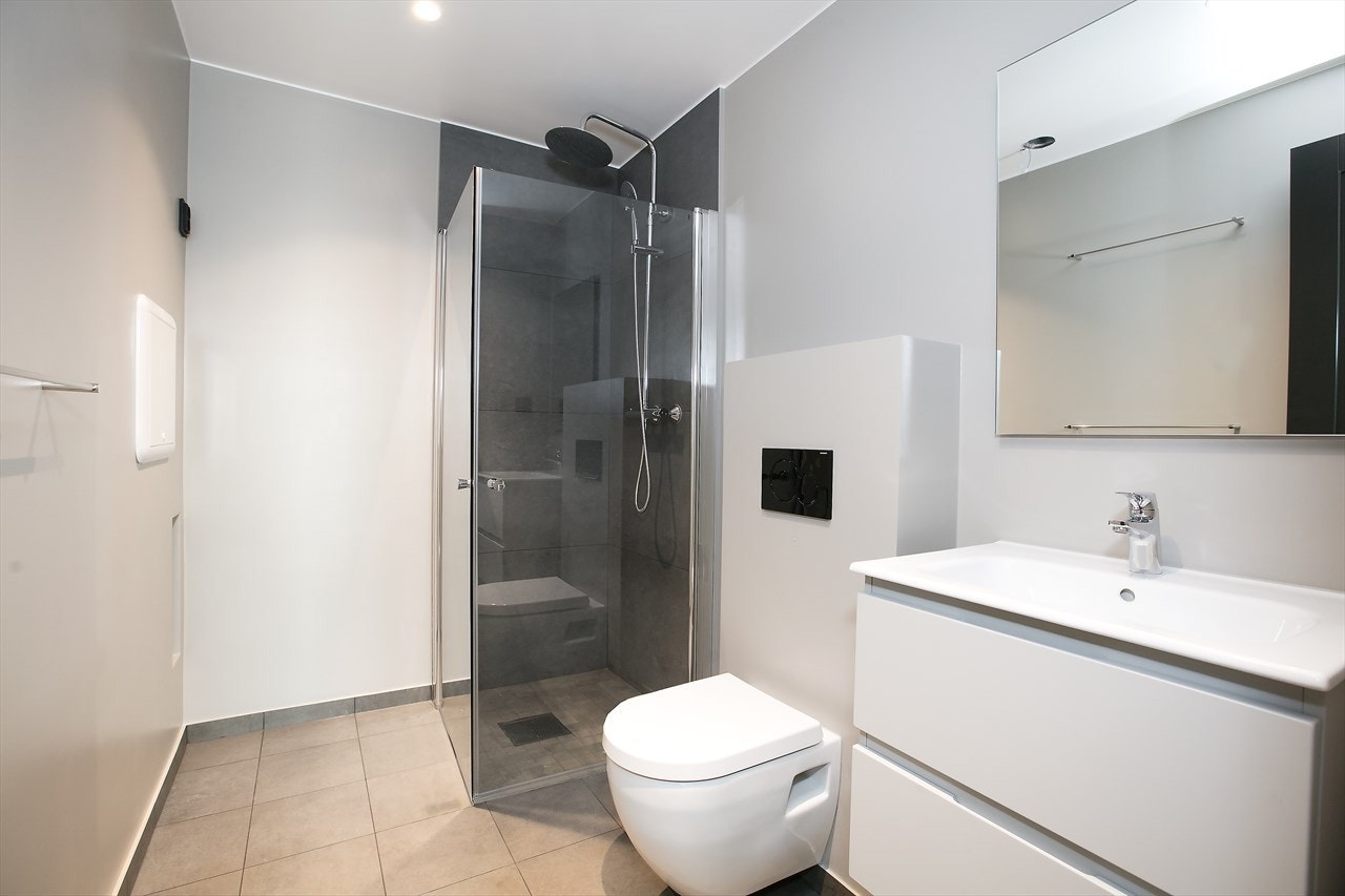 Badet i hybeldel er innredet med dusj med glassvegger, servant i innredning med skuffer under, speil/lys over servant, samt vegghengt toalett Galleribilde