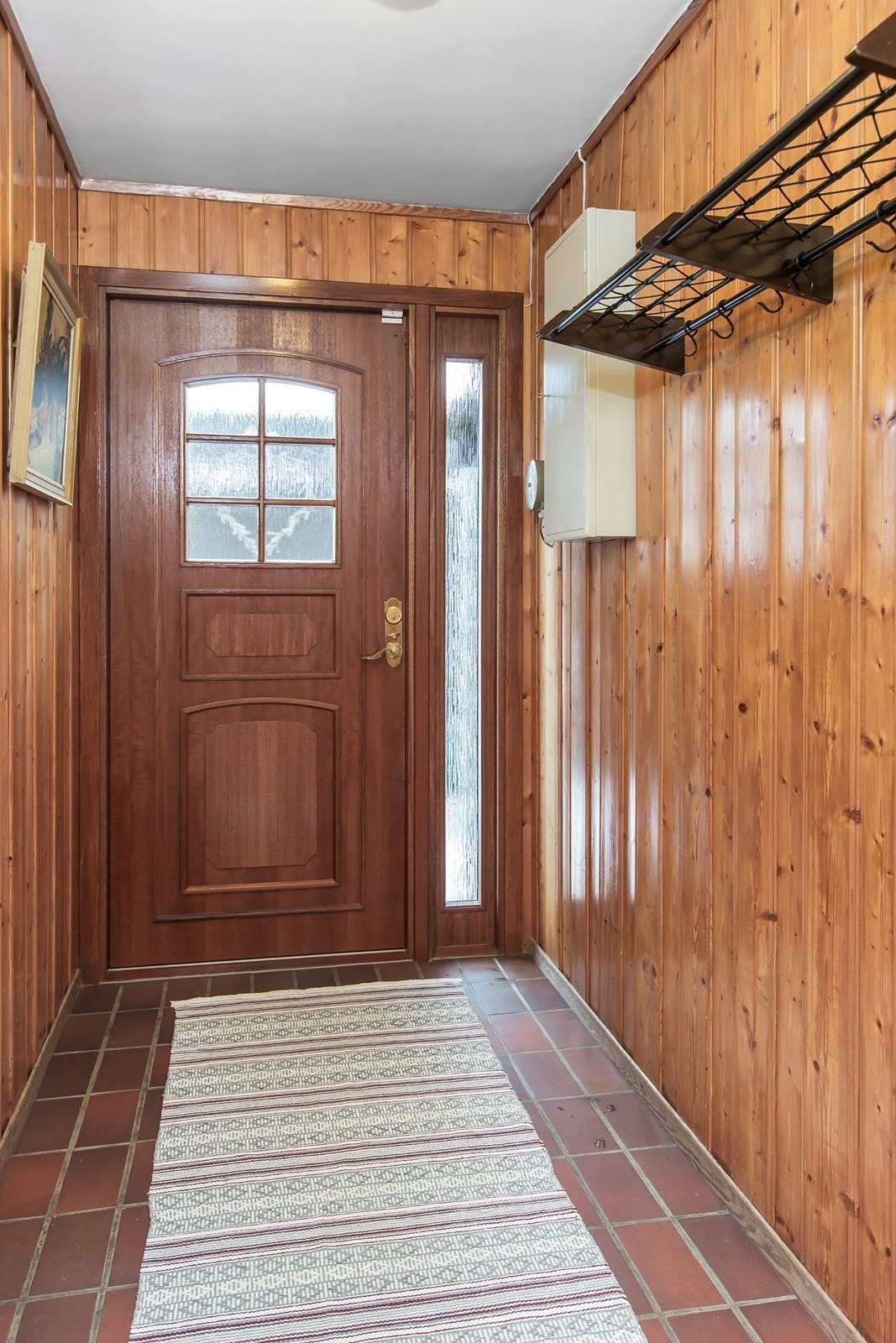 Innenfor ytterdøren er et vindfang med flisgulv og kvistpanel. Galleribilde