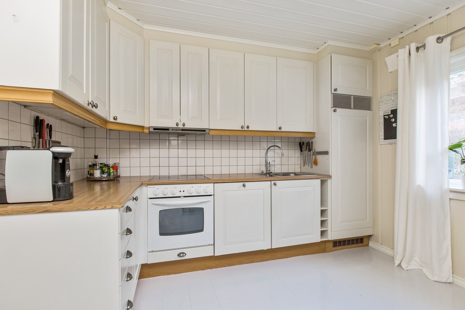 Kjøkken med hvit profilert innredning, integrert komfyr, platetopp og oppvaskmaskin. Ventilator. Galleribilde