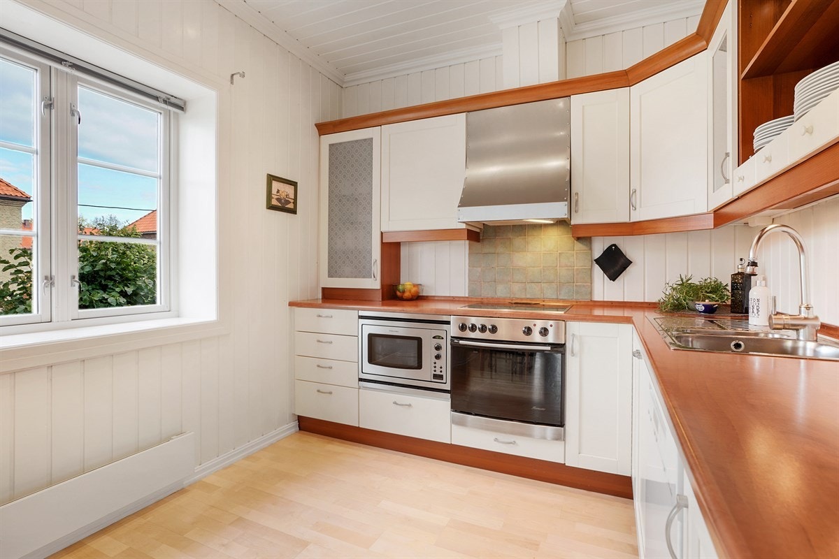 Store vindusflater slipper inn fint dagslys og gjør kjøkkenet lyst og åpent. Norema kjøkkeninnredning fra ca. 2000, med malte fronter, 3 fronter med glassfelt. Godt vedlikeholdt. Galleribilde