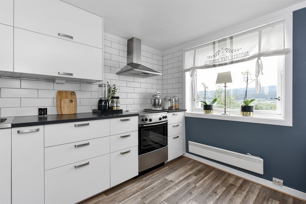 Over mørk laminatbenkeplate med oppvaskkum er det hvite fliser opp til taket, vegghengt ventilator i stål og horisontale overskap. Galleribilde