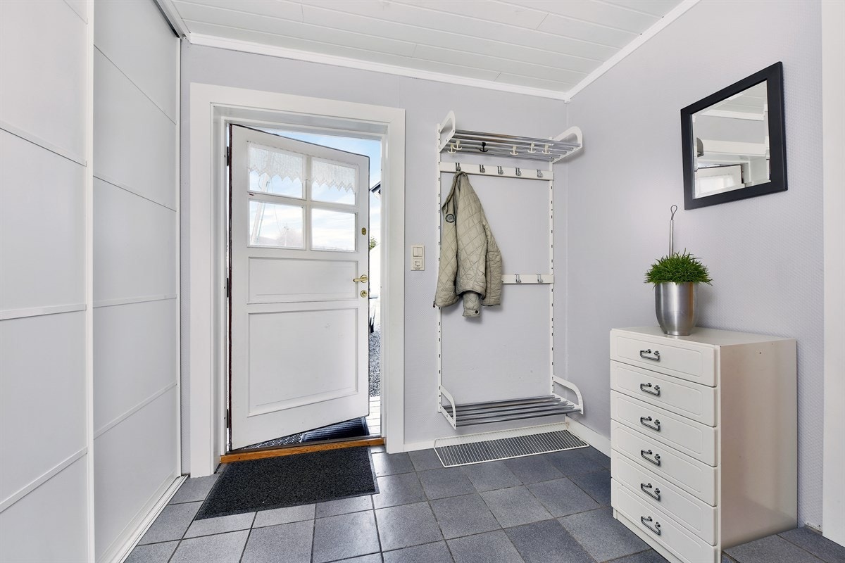 Entreen har flisegulv med gulvvarme, gråmalte vegger og en skyvedørsgarderobe med hvite fronter. Galleribilde