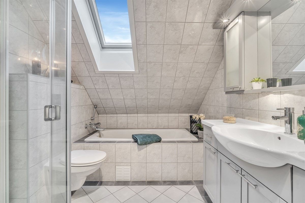 Badet i loftsetasjen har velholdte fliser, gulvvarme og et innfliset badekar under skråtak. Galleribilde