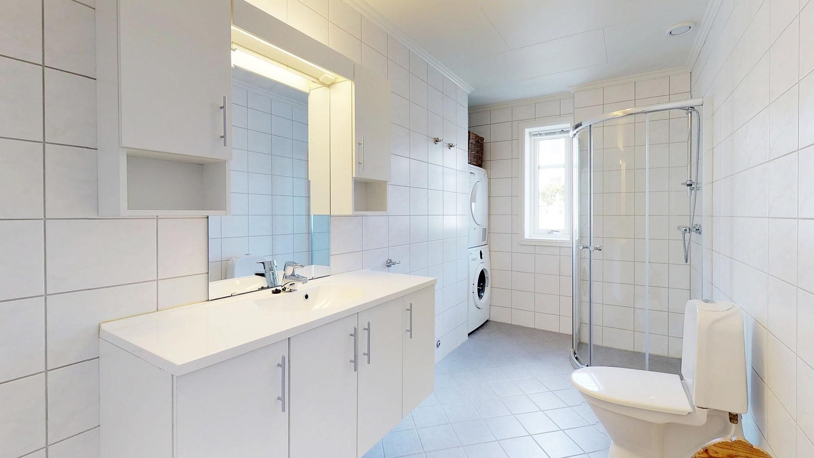 Romslig bad med fliser på gulv og vegg. Det er laget en egen huk til vaskemaskin og tørketrommel Galleribilde