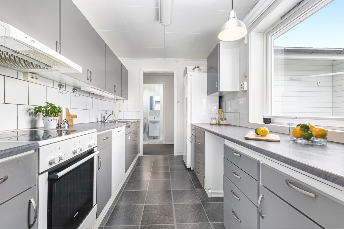 Kjøkken med god lagringsplass i over og underskap, dobbel oppvaskkum og flislagt vegg over benkeplate av laminat