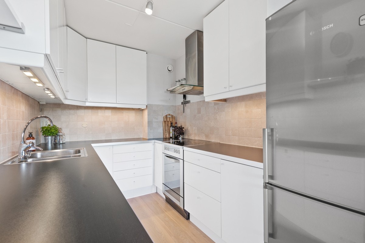 Funksjonelt kjøkken med fliser i sprutsonen, laminat benkeplate, grytekarussel i hjørne og LED-lys under overskap m.m. Galleribilde