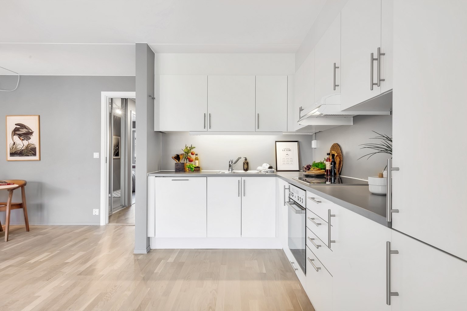 Laminert benkeplate med innfelt kjøkkenvask. Malt vegg over kjøkkenbenk. Integrerte hvitevarer med innfelt platetopp i benkeplate, nyere oppvaskmaskin, komfyr og kjøl/frys. Galleribilde