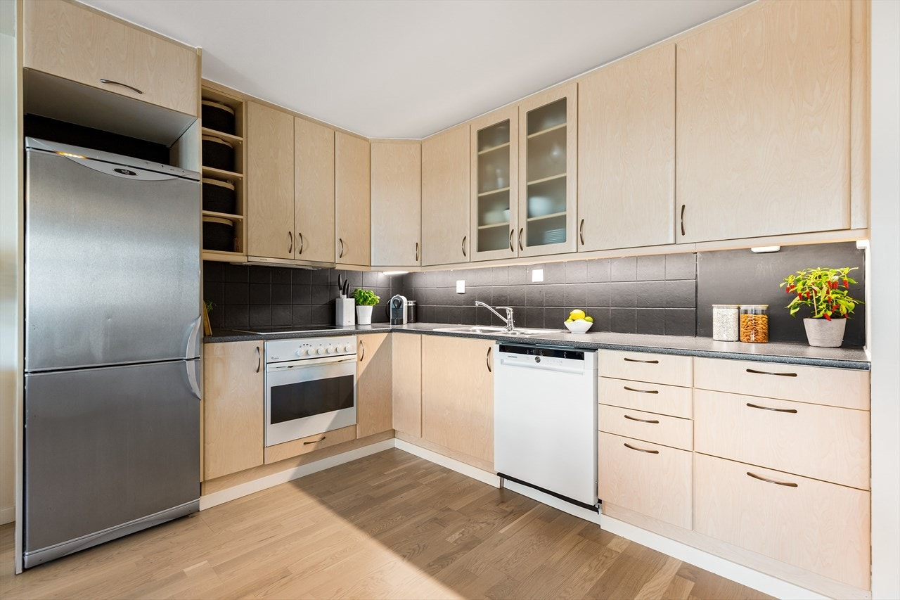 Kjøkkeninnredning med glatte fronter, takhøye overskap, benkeplate med nedfelt vaskekum og keramisk platetopp Galleribilde