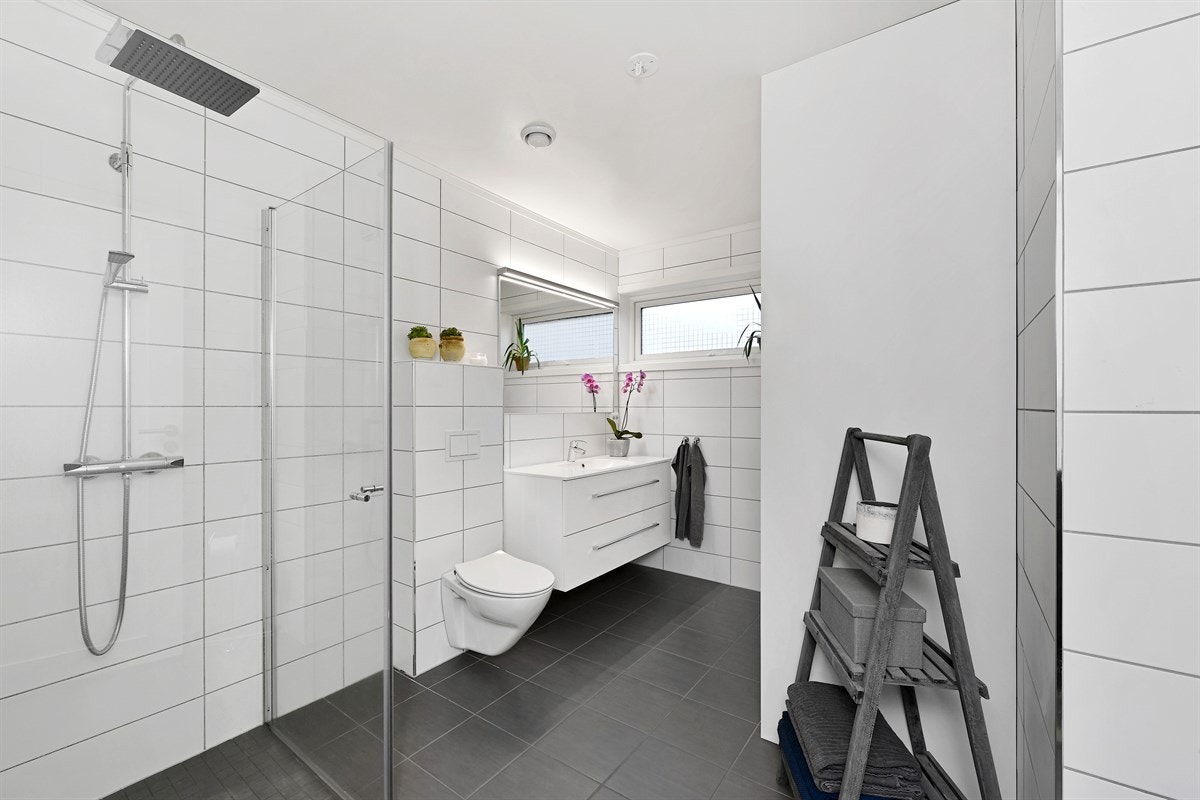 Badet har mørke gulvfliser, lyse veggfliser, gulvvarme og frostet vindu for lysinnslipp. Galleribilde
