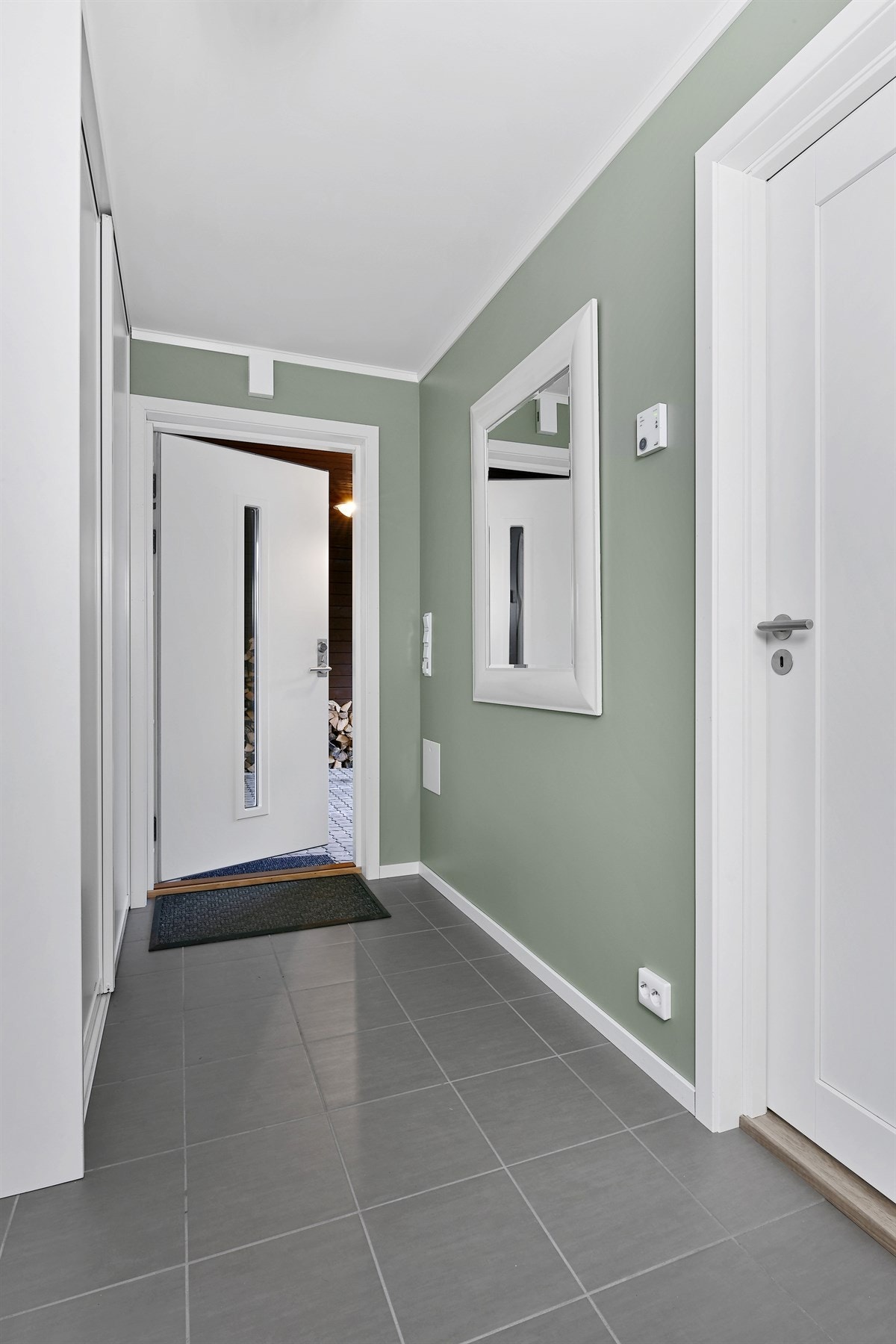 Inne i boligen møter du en meget pen entré med flislagt gulv, grønnmalte veggflater, gulvvarme og hvit inngangsdør med langsgående glassfelt. Galleribilde