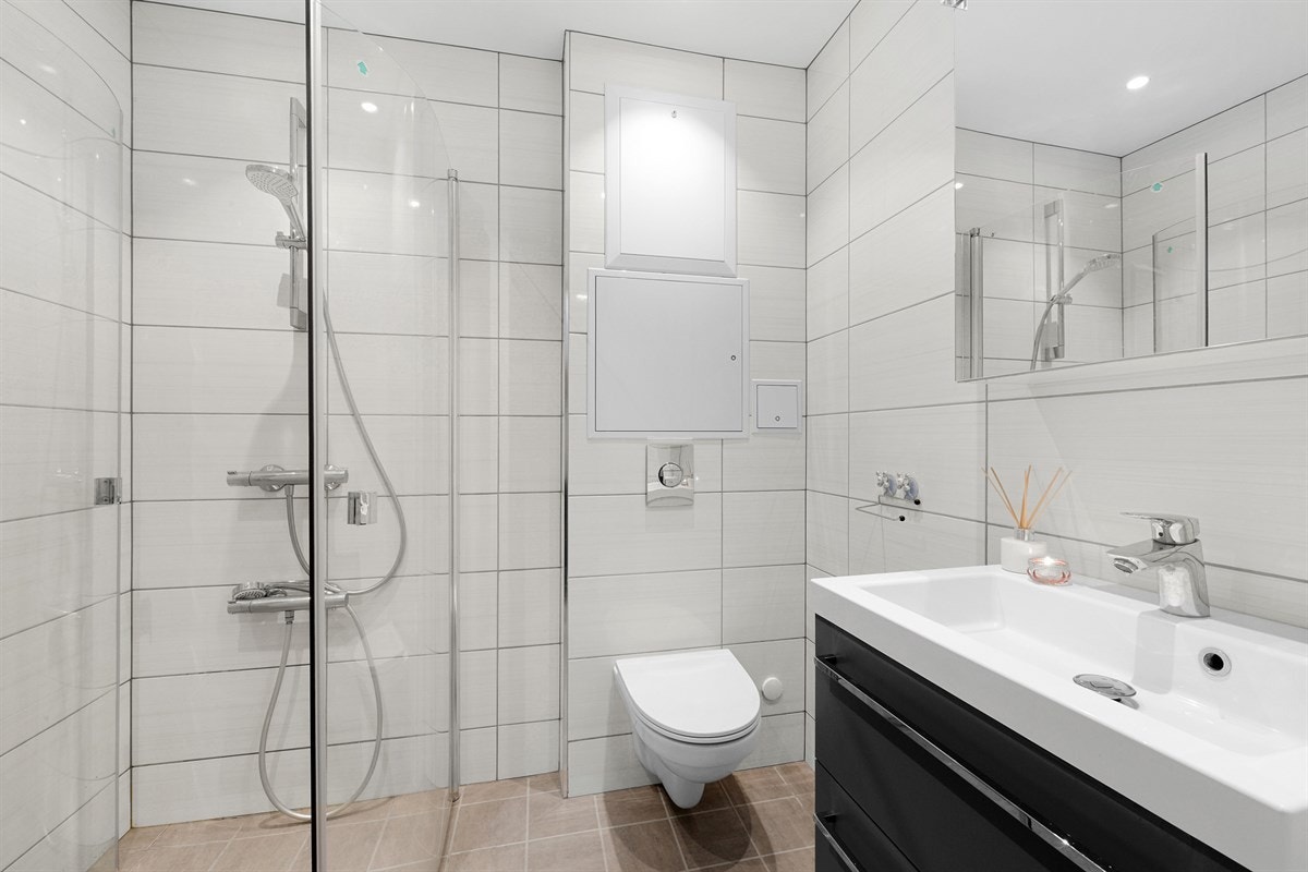 Badet i første etasje har hvite veggfliser som står i delikat kontrast til beige gulvfliser med varme. Galleribilde