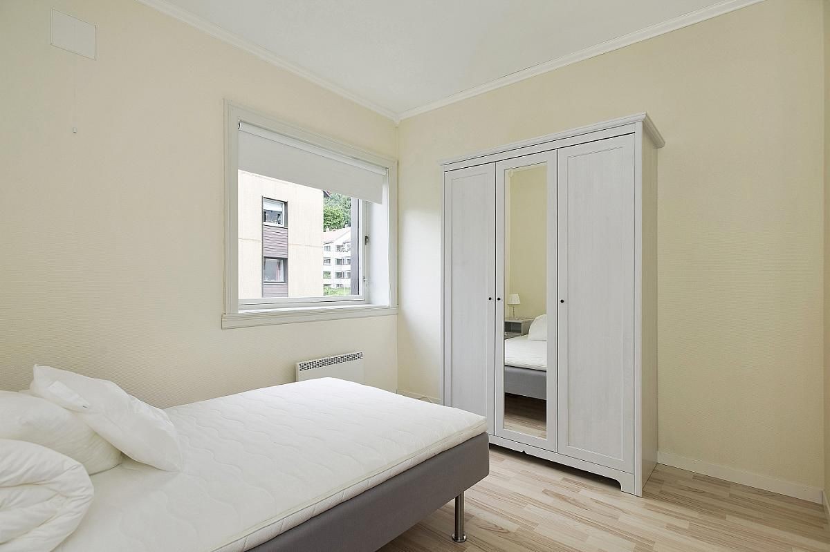 Lyst soverom møblert med seng og garderobe Galleribilde