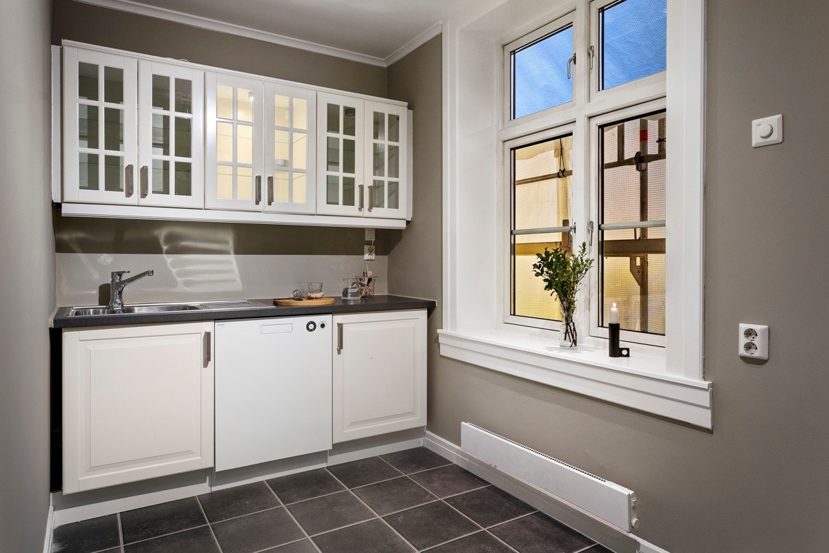 Separat og romslig kjøkken med kjøkkeninnredning av profilerte, sprøytelakkerte fronter og vitrinedører. Galleribilde