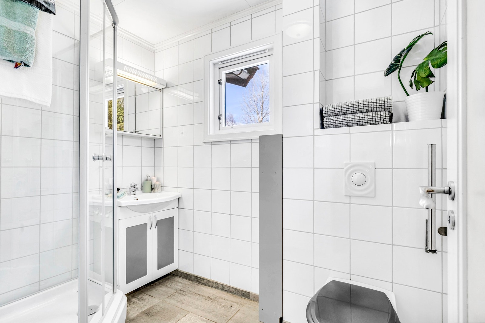 Bad i 1.etasje med flislagte overflater på gulv og vegger. Utstyrt med dusjkabinett, WC og servant i servantskap. Galleribilde