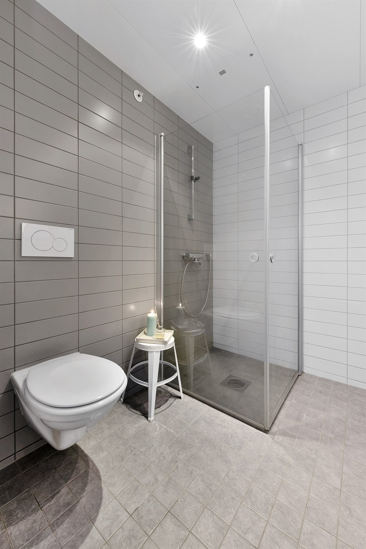 Badet fremstår med tidsmessige preg over overflater og innredning. Rommet har lysegrå småfliser på gulvet, hvite fliser på tre vegger, lysegrå fliser på fondvegg, vannbåren gulvvarme, downlights og balansert ventilasjon. Galleribilde