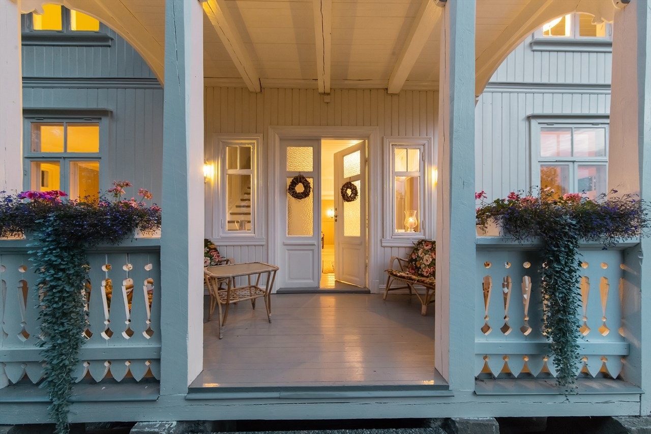 Hovedinngangen er innbydende, via verandaen ut mot hagen. Ytterdøren er tofløyet med store glassfelt og hallen på innsiden er vakker. Galleribilde