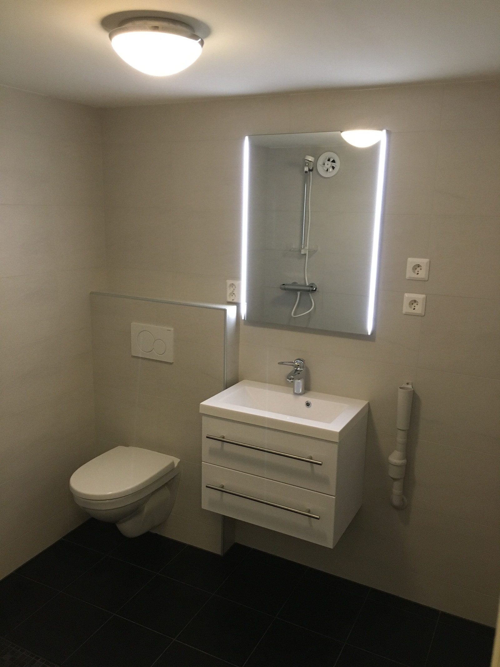 Nydelig flislagt bad med dusjhjørne, vegghengt toalett, vask og opplegg for vaskemaskin og tørketrommel. Galleribilde