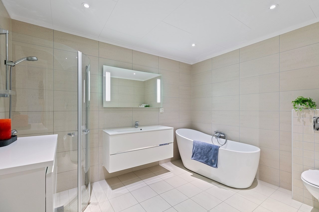 Badet i 1.etg har veggmontert toalett, dusjhjørne med buede, innfellbare glassdører og et lekkert badekar med dusjgarnityr. Galleribilde